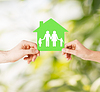 Manos que sostienen la casa verde con la familia | Foto de stock