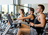 Los hombres que se resuelve en la bici de ejercicio en el gimnasio | Foto de stock