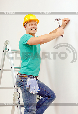 Smiling man in helmet hammering nail in wall | High resolution stock photo |ID 4453594